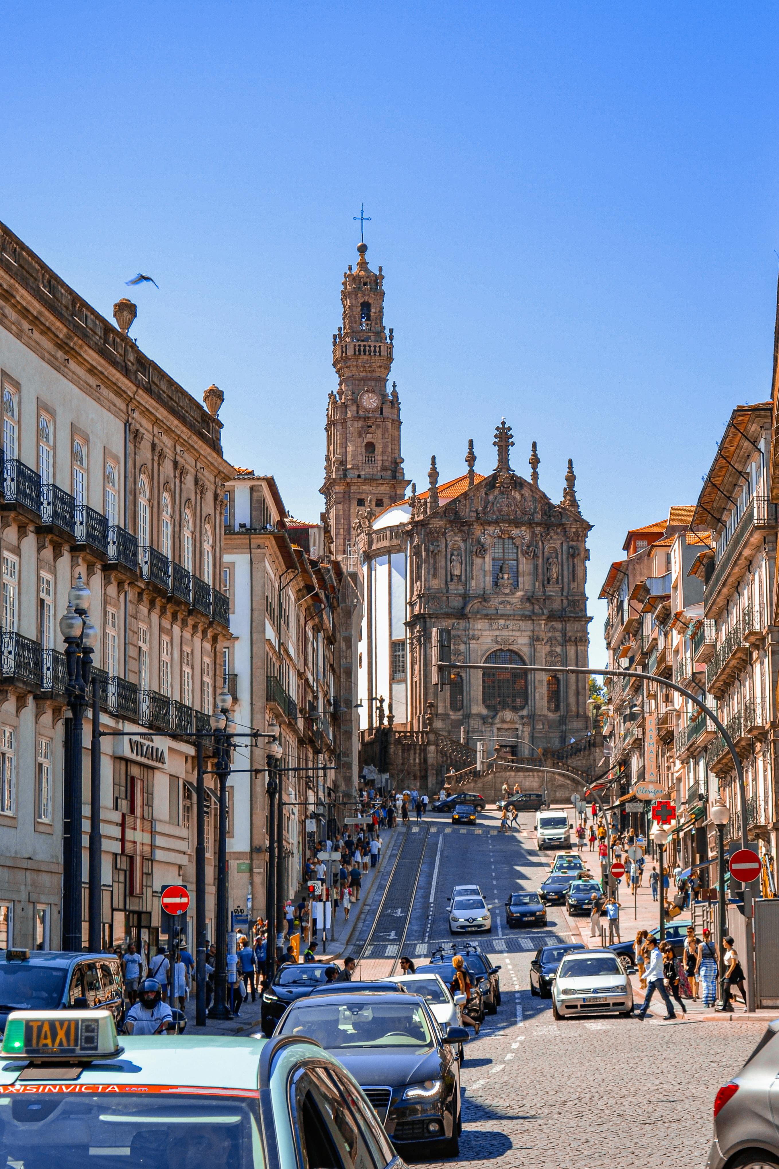 Rua movimentada no Porto com táxis e carros em circulação, com a Torre dos Clérigos ao fundo