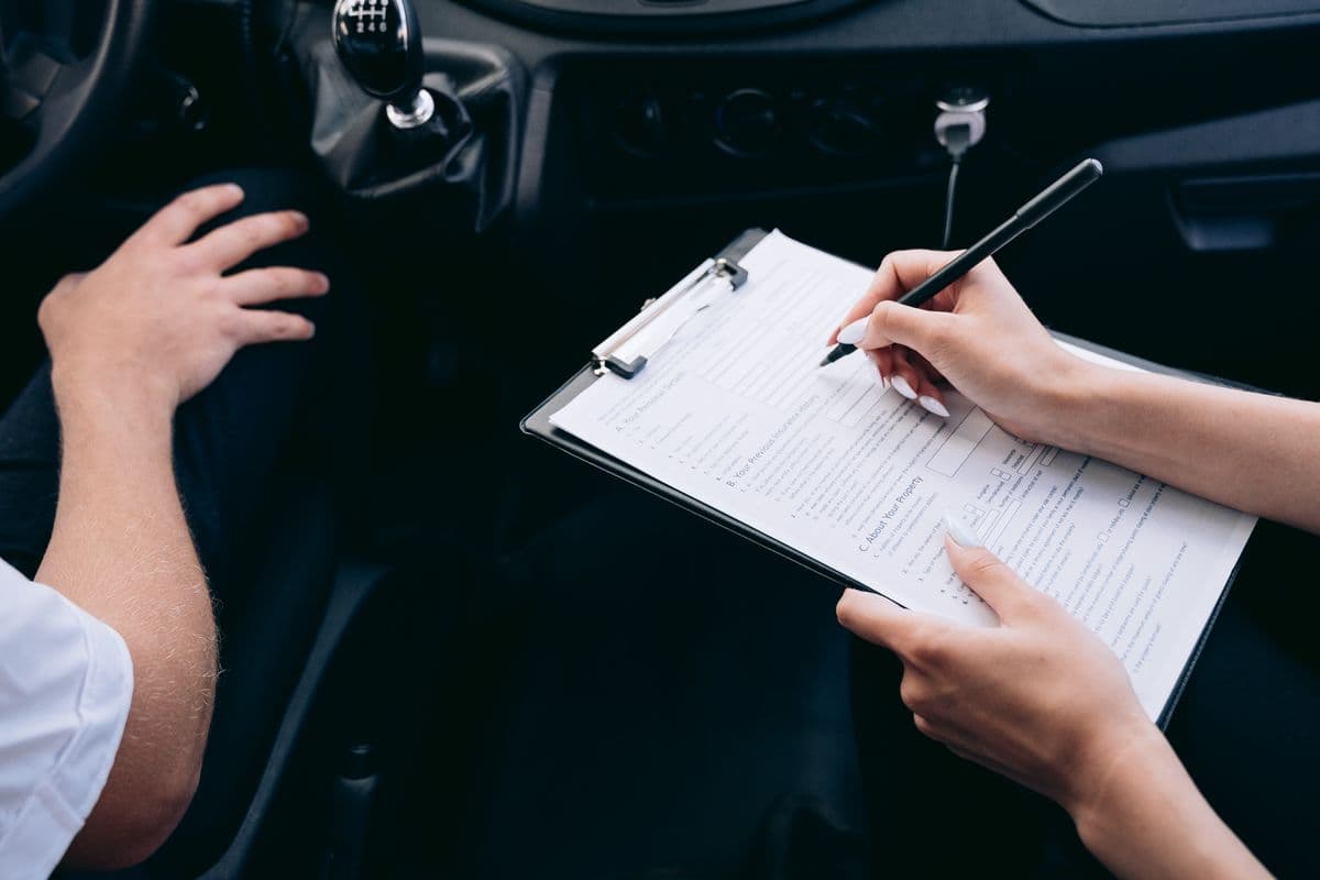 Mão a preencher um formulário de apólice de seguro numa prancheta, dentro de um automóvel