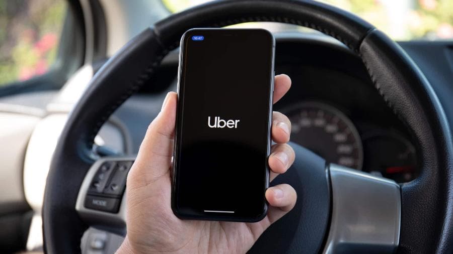 Mão a segurar smartphone com a app Uber aberta, com volante ao fundo